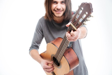 Attractive smiling young man with long hair playing acoustic guitar over white backgroundの写真素材