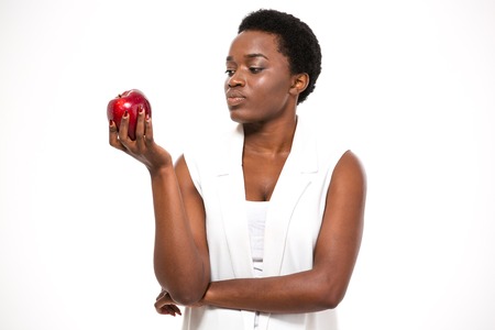 Pensive attractive african american young woman holding apple and thinking over white backgroundの写真素材