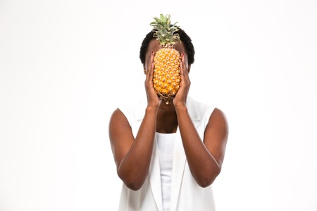 Portrait of african american young woman covered her face with pineapple over white backgroundの写真素材