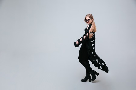 Full length portrait of a female model posing in fashion loth and sunglasses over gray backgroundの写真素材