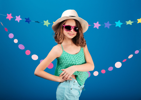 Cheerful cute little girl in sunglasses standing and posing over blue backgroundの写真素材