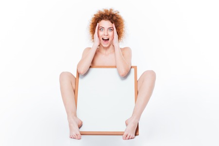 Amazed naked woman sitting with blank board isolated on a white backgroundの写真素材