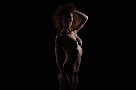 Silhouette of a beautiful nude woman standing on black backgroundの写真素材
