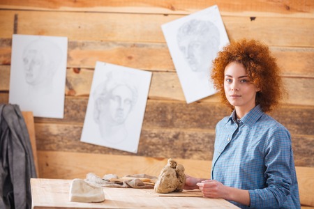 Beautiful redhead woman potter sitting and working with clay in workshopの写真素材