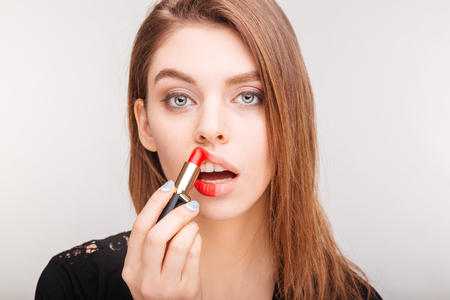 Beauty portrait of pretty young woman doing makeup with red lipstick over white backgroundの写真素材