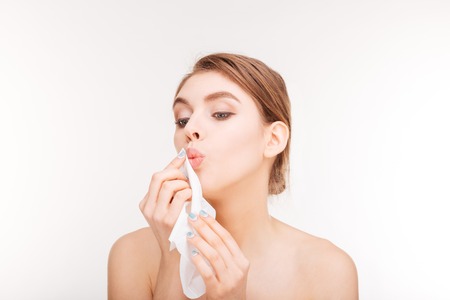 Beauty portrait of cute lovely young woman applying paper napkin to her lips over white backgroundの写真素材