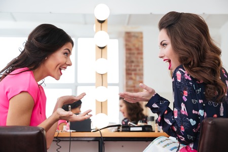 Two surprised young women sitting and talking in beauty salonの写真素材