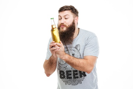 Hansome amusing man with beard holding bottle of beer and looking on it over white backgroundの写真素材