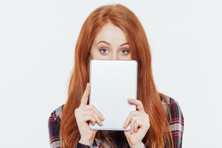 Redhead woman peeking from tablet computer isolated on a white background