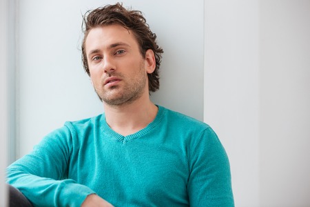 Portrait of handsome relaxed young man in blue jumper over white background