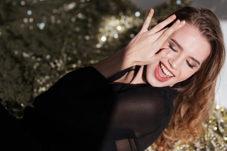 Smiling charming young woman in black dress with closed eyes over glittering backgroundの写真素材