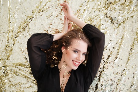 Top view of happy beautiful young woman with sequins on her face lying and smiling over sparkling backgroundの写真素材