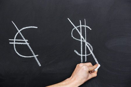 Signs of euro and dollar crossed on blackboard by hand with chalkの写真素材