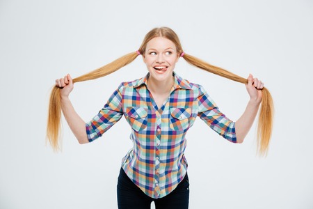 Funny young woman holding her ponytail and showing tongue isolated on a white background