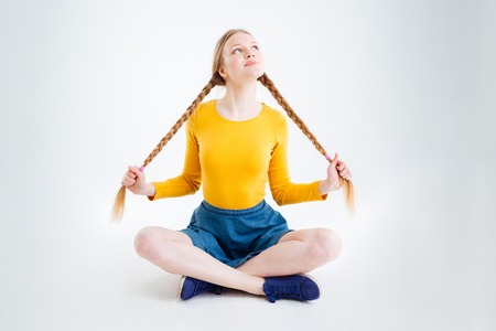 Happy thoughtful girl sitting on the floor and looking up isolated on a white backgroundの写真素材
