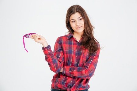 Smiling cute young woman in checkered shirt standing and holding sunglasses over white backgroundの写真素材
