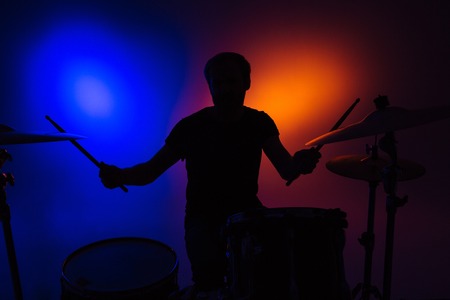 Silhouette of man drummer sitting and playing drums with sticks over colorful backgoundの写真素材