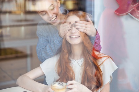 Happy charming young woman closed eyes to her female friend in cafeの写真素材