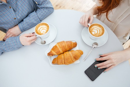 Top view of two women drinking coffee with croissants on white round tableの写真素材