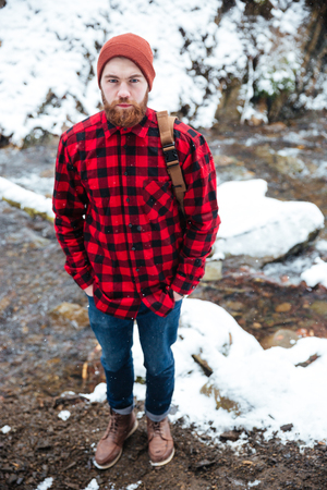 Top view of handsome bearded young man with backpack standing in winter forest near mountain riverの写真素材
