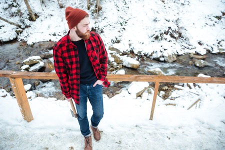 Top view of handsome thoughtful young man with axe standing and looking on small mountain riverの写真素材