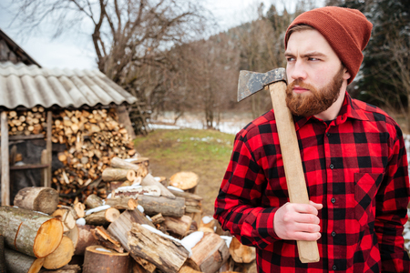 Serious lumberjack holding axe and looking away outdoorsの写真素材