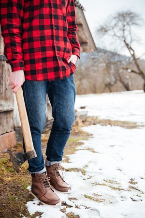 Man in plaid shirt and jeans standing and holding axe in villageの写真素材