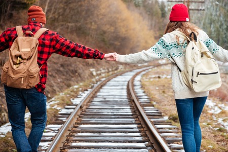 Beautiful young couple with backpacks holding hands and walking along railroad togetherの写真素材