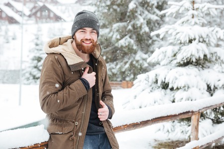 Happy bearded young man standing and smiling in wintertime outdoors