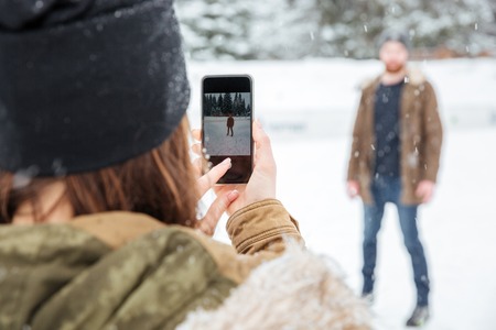 Woman making photo of a man outdoors with snow on background