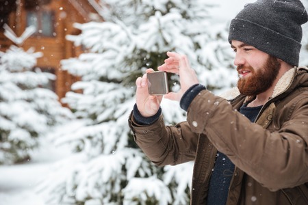 Attractive bearded man taking pictures with mobile phone in winterの写真素材