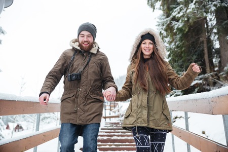 Happy young couple holding hands and running down the stairs in winterの写真素材