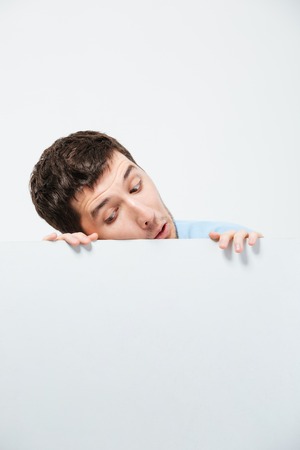Young man peeking from blank board isolated on a white backgroundの写真素材