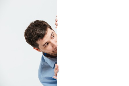 Businessman peeking from blank board isolated on a white backgroundの写真素材