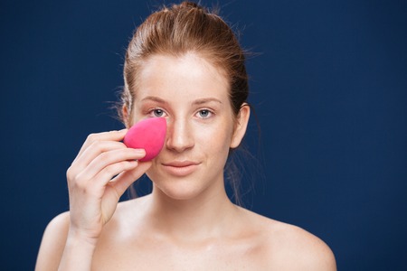 Beauty portrait of a woman applying makeup with sponge over blue backgroundの写真素材