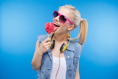 Cheerful female teenager holding lollipop over blue backgoundの写真素材