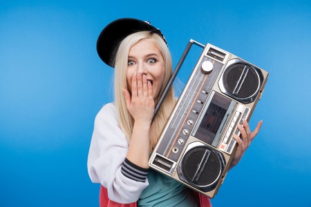 Happy female teenager holding retro boom box on blue background