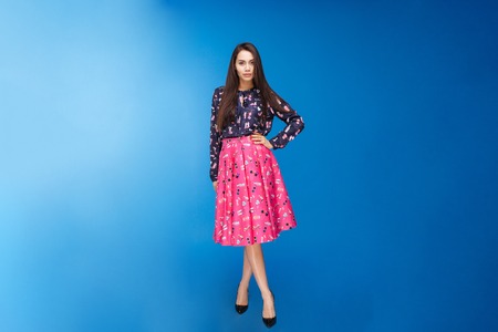 Full length portrait of a beautiful woman in fashion dress standing over blue backgroundの写真素材