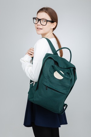 Happy pretty teenage girl in glasses with backpack standing and looking back