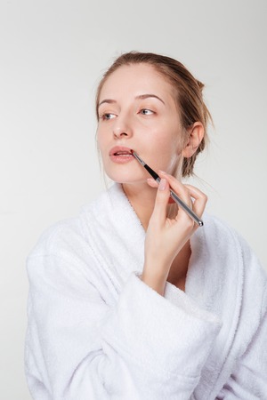Woman applying lipstick with an applicator isolated on a white background and looking awayの写真素材