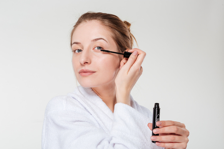 Beautiful woman applying mascara on eyelashes isolated on a white backgroundの写真素材