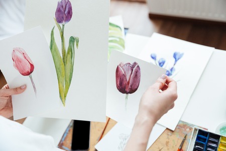Hands of woman painter holding pisctures of flowers in art studioの写真素材