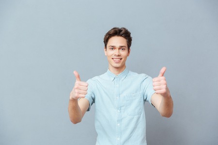 Smiling man showing thumbs up over gray backgroundの写真素材