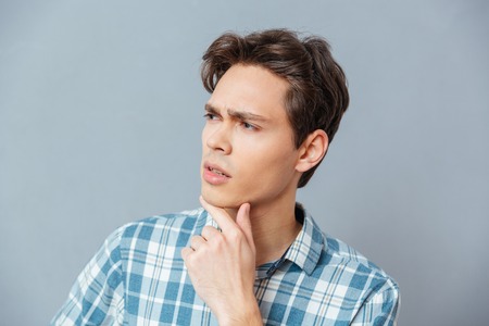 Pensive casual man looking away over gray backgroundの写真素材