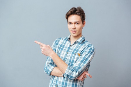 Young man pointing finger away over gray backgroundの写真素材