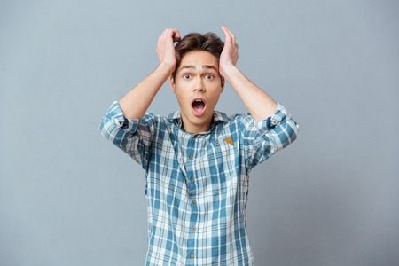 Amazed casual man looking at camera over gray backgroundの写真素材