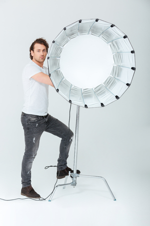Full length portrait of a handsome man preparing lighting equipment isolated on a white backgroundの写真素材
