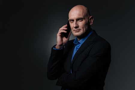 Serious attractive businessman talking on mobile phone over black backgroundの写真素材