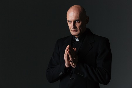 Priest standing and praying over black backgroundの写真素材