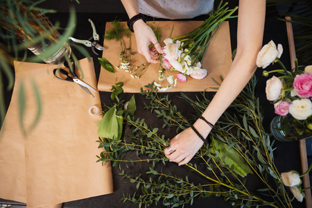 Top view of hands of young woman florist creating bouquet of flowers on black tableの写真素材